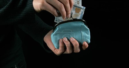Photo for Hand of Woman putting Dollar Banknotes into Blue Purse - Royalty Free Image