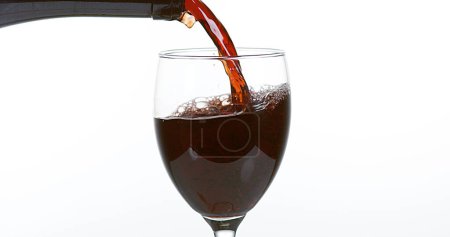 Foto de Vino tinto que se vierte en vidrio, contra fondo blanco - Imagen libre de derechos