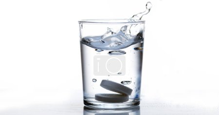 Téléchargez les photos : Comprimés tombant et se dissolvant dans un verre d'eau sur fond blanc - en image libre de droit