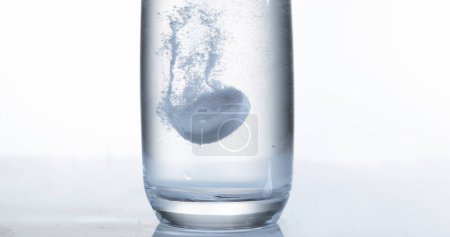 Foto de Tabletas cayendo y disolviéndose en un vaso de agua contra fondo blanco - Imagen libre de derechos