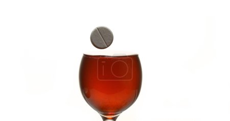 Foto de Tableta cayendo en una copa de vino tinto sobre fondo blanco - Imagen libre de derechos