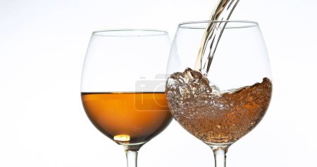 Foto de Vino rosado que se vierte en vidrio, contra fondo blanco - Imagen libre de derechos