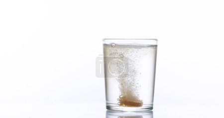 Foto de Tabletas cayendo y disolviéndose en un vaso de agua contra fondo blanco - Imagen libre de derechos