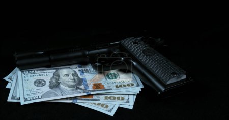 Foto de Pistola cayendo sobre billetes de 100 dólares estadounidenses sobre fondo negro - Imagen libre de derechos
