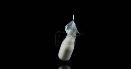 Téléchargez les photos : Bouteille de lait tombant et explosant sur fond noir - en image libre de droit