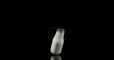 Foto de Botella de leche cayendo y explotando contra fondo negro - Imagen libre de derechos