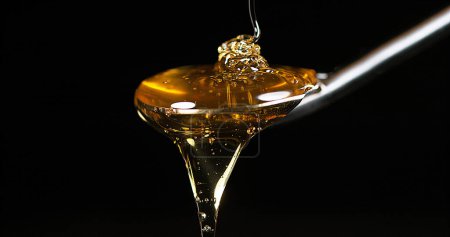Téléchargez les photos : Miel coulant sur cuillère sur fond noir - en image libre de droit