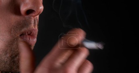 Foto de Hombre fumando un cigarrillo contra fondo negro - Imagen libre de derechos