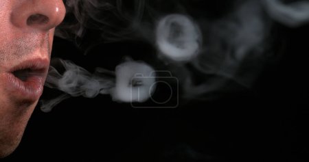 Téléchargez les photos : Homme fumant une cigarette sur fond noir - en image libre de droit