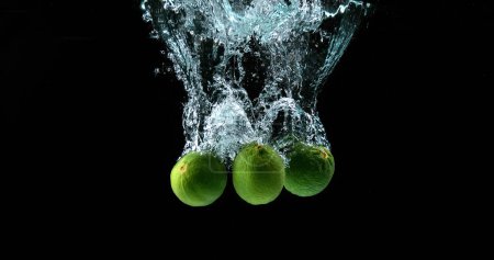 Foto de Limones verdes, cítricos aurantifolia, frutas que caen al agua contra el fondo negro - Imagen libre de derechos