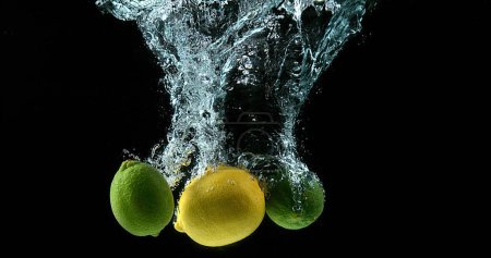 Foto de Cítricos amarillos y verdes, cítricos limonum, cítricos aurantifolia, frutas que caen al agua contra el fondo negro - Imagen libre de derechos