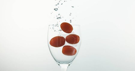 Téléchargez les photos : Tomates cerises, solanum lycopersicum, Fruits tombant dans l'eau sur fond blanc - en image libre de droit
