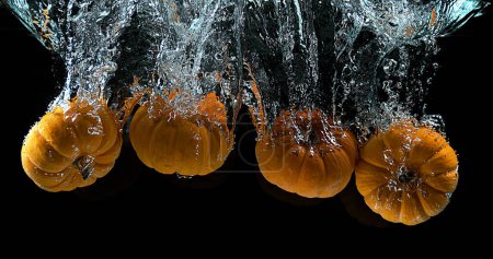 Foto de Calabaza enana, cucurbita pepo, Fruta cayendo en el agua contra el fondo negro - Imagen libre de derechos