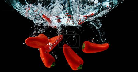 Foto de Pimientos dulces rojos, capsicum annuum, verduras cayendo en el agua contra el fondo negro - Imagen libre de derechos