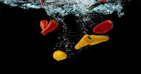 Téléchargez les photos : Poivrons rouges et jaunes, Capsicum annuum, Légumes tombant dans l'eau sur fond noir - en image libre de droit