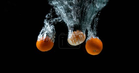 Téléchargez les photos : Clémentines, agrumes réticulés, fruits tombant dans l'eau sur fond noir - en image libre de droit