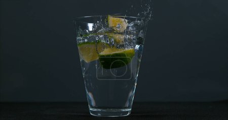 Foto de Cítricos verdes, cítricos aurantifolia, cayendo en un vaso de agua, - Imagen libre de derechos