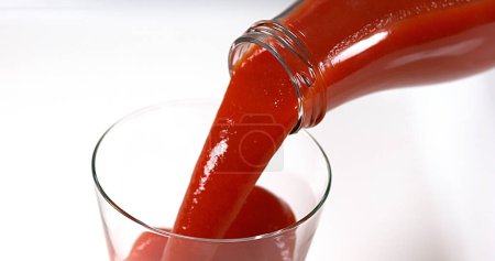 Foto de El jugo de tomate se vierte en un vaso contra fondo blanco - Imagen libre de derechos