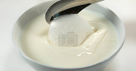 Foto de Cuchara de azúcar y tazón de leche contra fondo blanco - Imagen libre de derechos