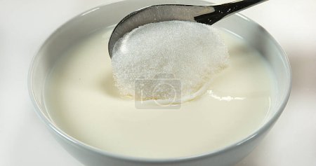 Foto de Cuchara de azúcar y tazón de leche contra fondo blanco - Imagen libre de derechos