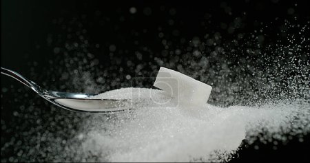 Téléchargez les photos : Cube de sucre blanc tombant sur le sucre en poudre sur fond noir - en image libre de droit