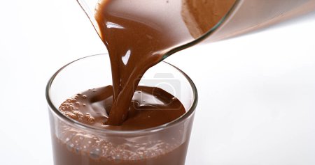 Foto de Chocolate vertiendo en un vaso contra fondo blanco - Imagen libre de derechos