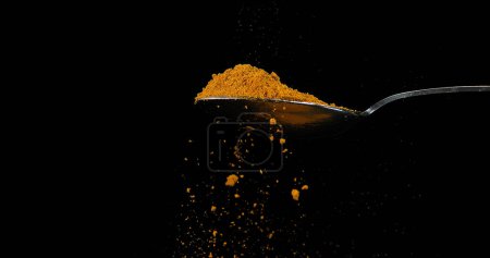 Foto de Cuchara y curry en polvo cayendo de la cuchara contra fondo negro - Imagen libre de derechos