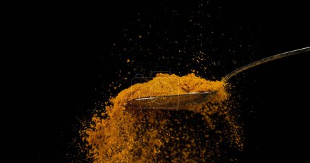 Photo for Spoon and Curry Powder falling from Spoon against Black Background - Royalty Free Image