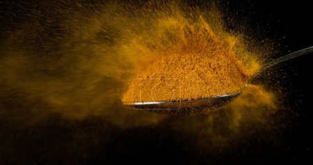 Foto de Cuchara y curry en polvo cayendo de la cuchara contra fondo negro - Imagen libre de derechos