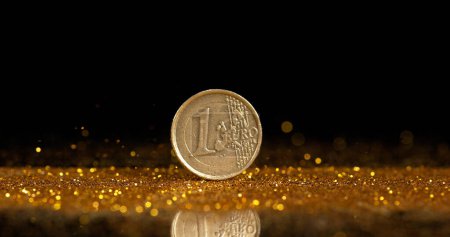 Foto de Moneda de 1 euro rodando en polvo de oro contra fondo negro - Imagen libre de derechos