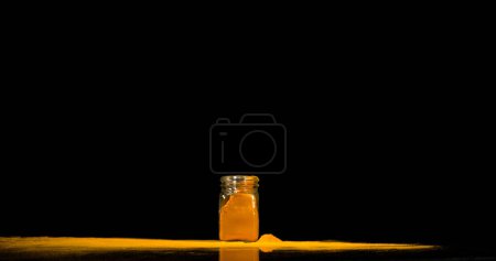 Photo for Turmeric, curcuma longa, Powder into a small jar falling against Black Background, Indian Spice - Royalty Free Image