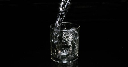 Foto de Agua que se vierte en vidrio contra fondo negro - Imagen libre de derechos