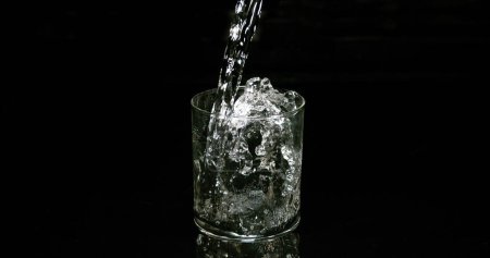 Foto de Agua que se vierte en vidrio contra fondo negro - Imagen libre de derechos