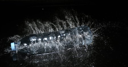 Téléchargez les photos : Bouteille d'eau tombant sur l'eau sur fond noir - en image libre de droit