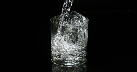 Téléchargez les photos : L'eau étant versée dans le verre sur fond noir - en image libre de droit