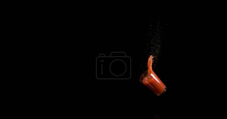 Téléchargez les photos : Verre de jus de tomate rebondissant et éclaboussant sur fond noir - en image libre de droit