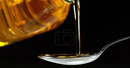 Foto de Aceite de oliva vertiendo de cuchara sobre fondo negro. - Imagen libre de derechos