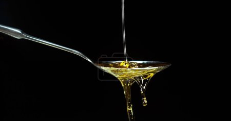 Photo for Olive Oil, Falling in a Spoon against Black Background - Royalty Free Image