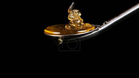 Téléchargez les photos : Miel coulant de cuillère sur fond noir - en image libre de droit