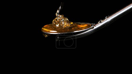 Photo for Honey Flowing from Spoon against Black Background - Royalty Free Image