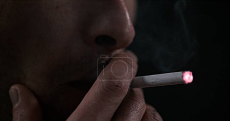 Téléchargez les photos : Homme fumant une cigarette sur fond noir - en image libre de droit