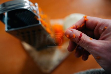 Foto de A woman cut her finger until it bled on a grater while cooking dinner. High quality photo - Imagen libre de derechos