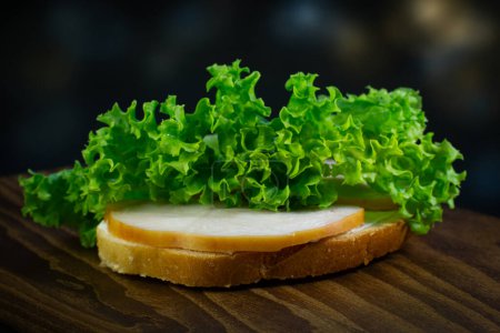 Frisches Sandwich mit Schinken und Salatblatt auf dem Holzbrett, dunkler Hintergrund