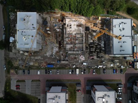 Aerial View of Residential Construction Site with Two Working Cranes An aerial view, reminiscent of map views, captures the construction of three residential blocks with two active cranes. The site is cluttered with a substantial amount of constructi