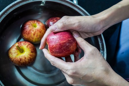 Photo for Woman hand is cleaning red apple in bucket of water, closed up shot - Royalty Free Image