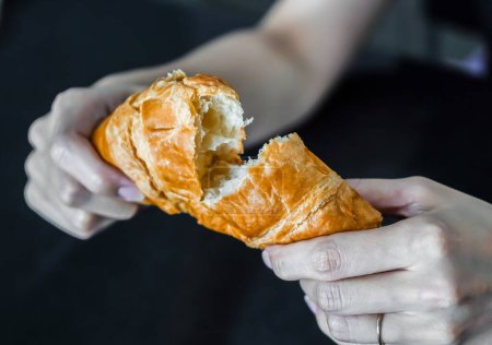 Photo for Woman tearing and breaking a croissant in her hand, closed up shot. - Royalty Free Image
