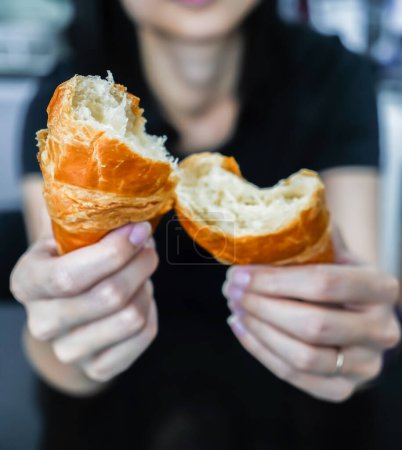 Photo for Woman tearing and breaking a croissant in her hand, closed up shot. - Royalty Free Image