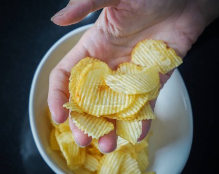 Photo for Woman using her hand to pick up potato chips from a bowl, closed up shot. - Royalty Free Image