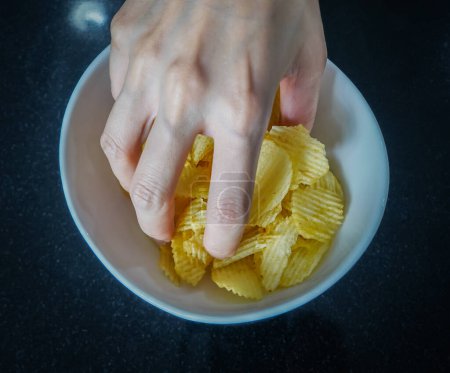 Photo for Woman using her hand to pick up potato chips from a bowl, closed up shot. - Royalty Free Image