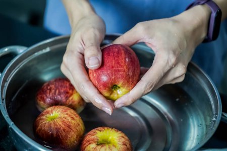 Photo for Woman hand is cleaning red apple in bucket of water, closed up shot - Royalty Free Image